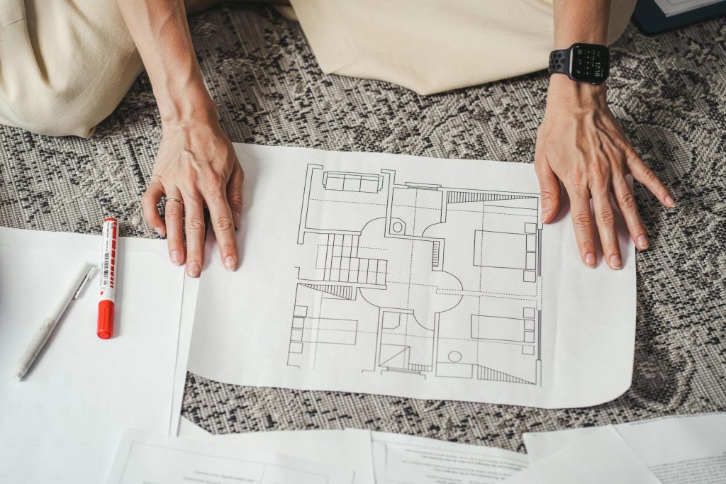 Hände an einem detaillierten Architekturplanpapier, das die Raumaufteilung des Hauses zeigt.