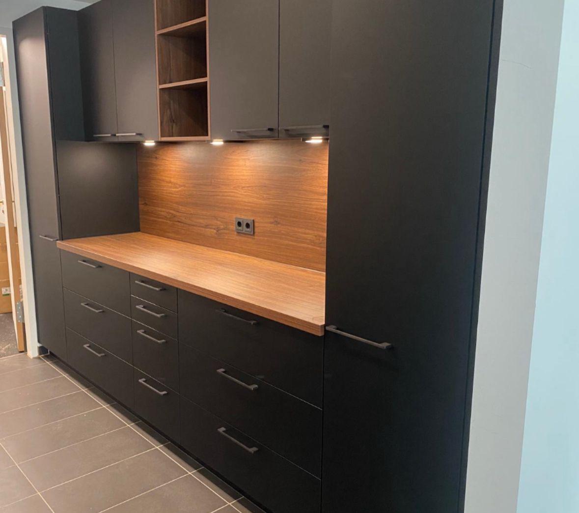 Elegante mattschwarze Küchenzeile mit Unterbau-Beleuchtung, integrierten Regalen und einer Rückwand sowie Arbeitsfläche aus warmem Holz.