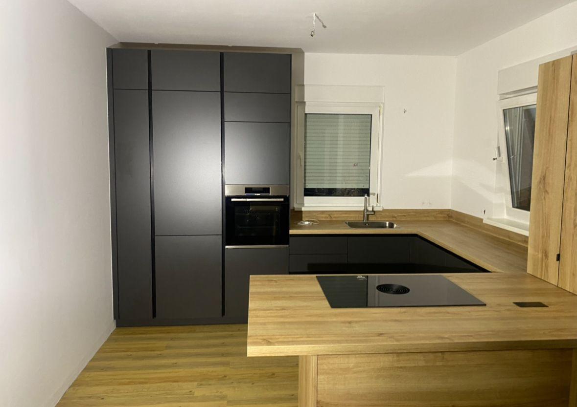 Moderne, dunkle Einbauküche in U-Form mit Holz-Arbeitsplatte, integriertem Backofen auf Augenhöhe und Parkettboden.