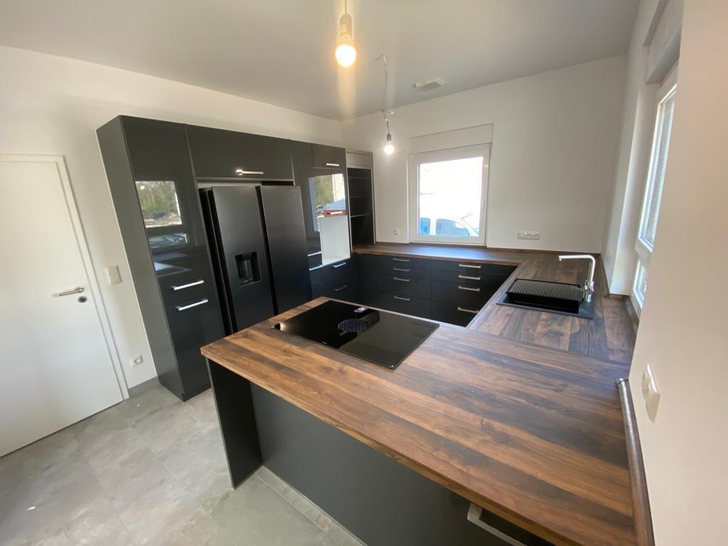 Moderne U-Küche in Schwarz und Holzoptik mit großem Side-by-Side-Kühlschrank und Induktionskochfeld.