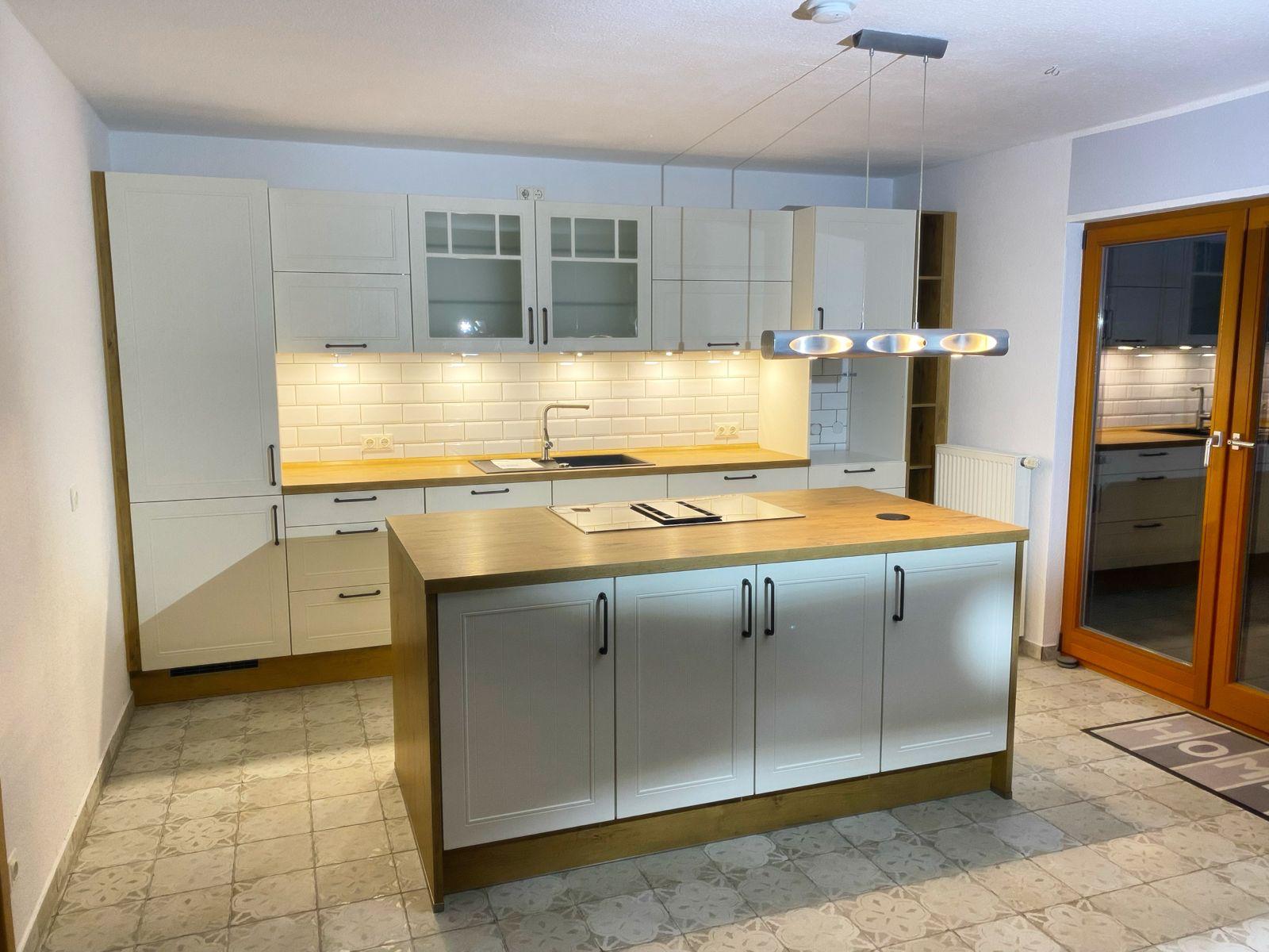 Gemütliche Landhausküche in Beige mit Holz-Arbeitsplatten, Kochinsel, weißem Fliesenspiegel und moderner Hängeleuchte